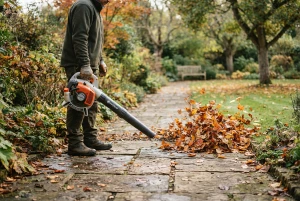 Laubbläser bündelt Laub zu einem Haufen auf einem Gartenweg